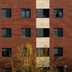 Close-up of a brick and concrete residential building facade in Logroño with symmetrical windows and trees below.